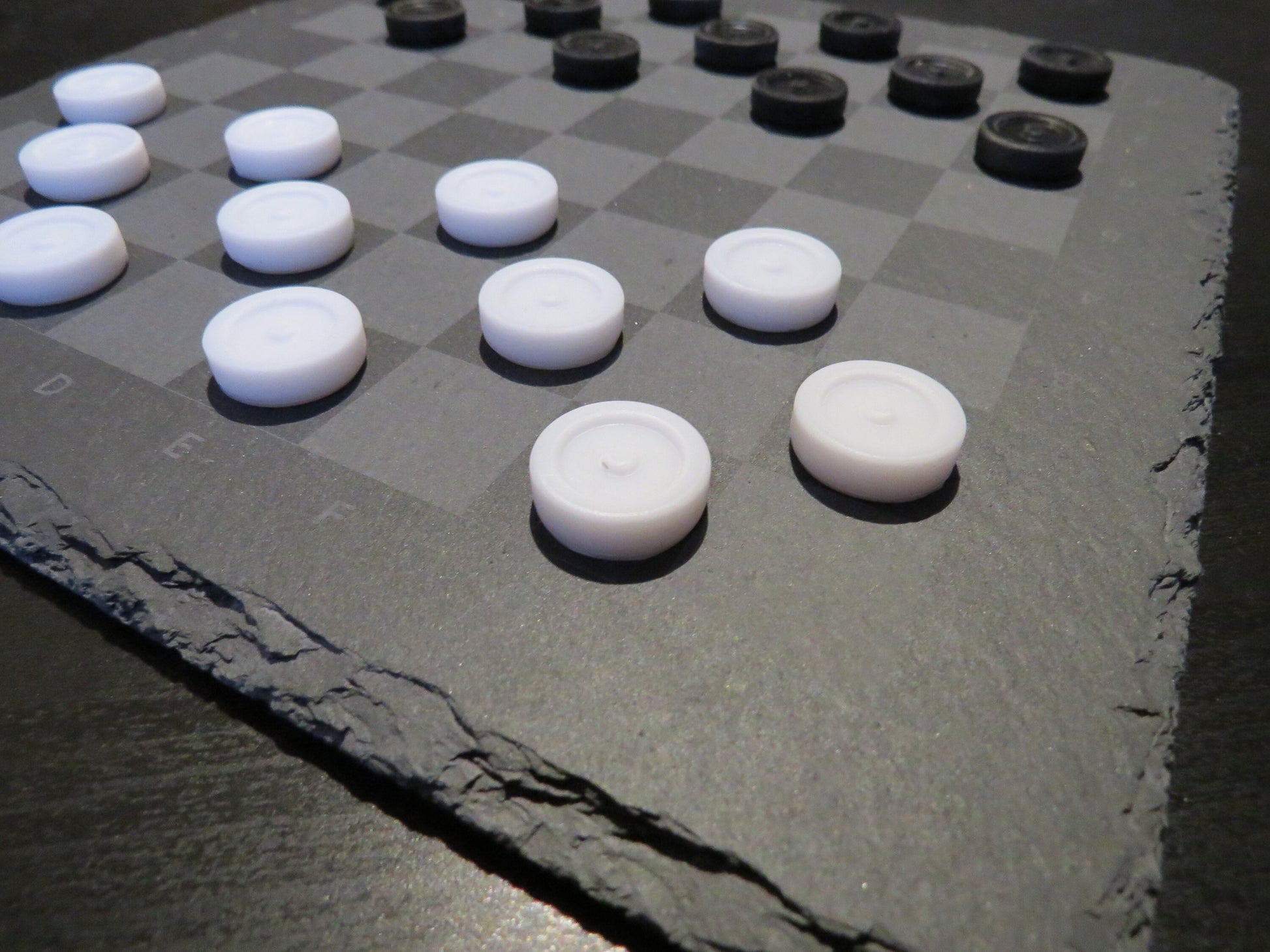 Nahaufnahme Dame Spielsteine: Strukturierte Schieferoberfläche mit lasergraviertem Raster und flachen Spielsteinen.