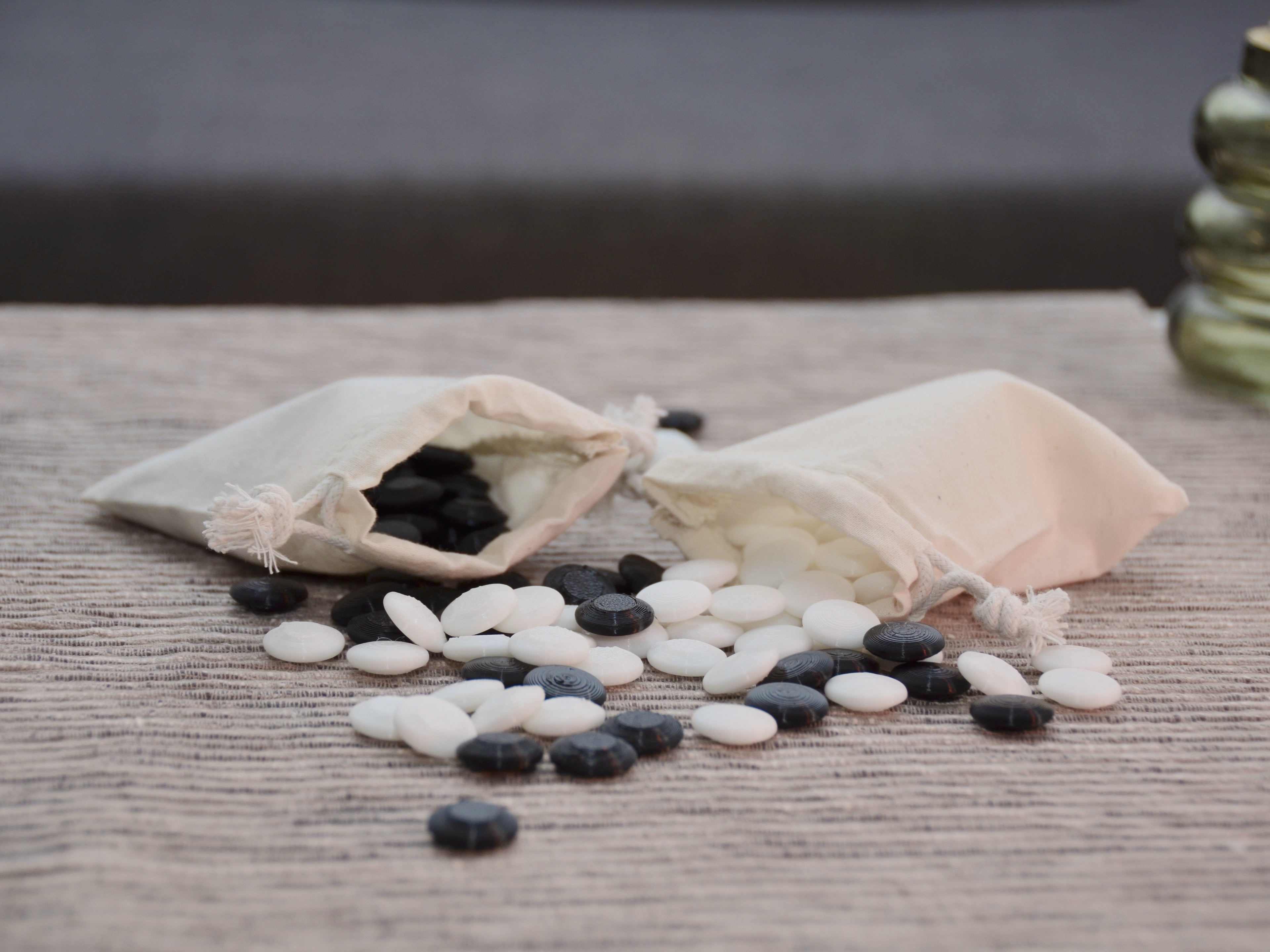 Go Spielsteine Zubehör: Jutesäckchen mit herausfallenden schwarzen und weißen Steinen auf dem Schieferbrett.