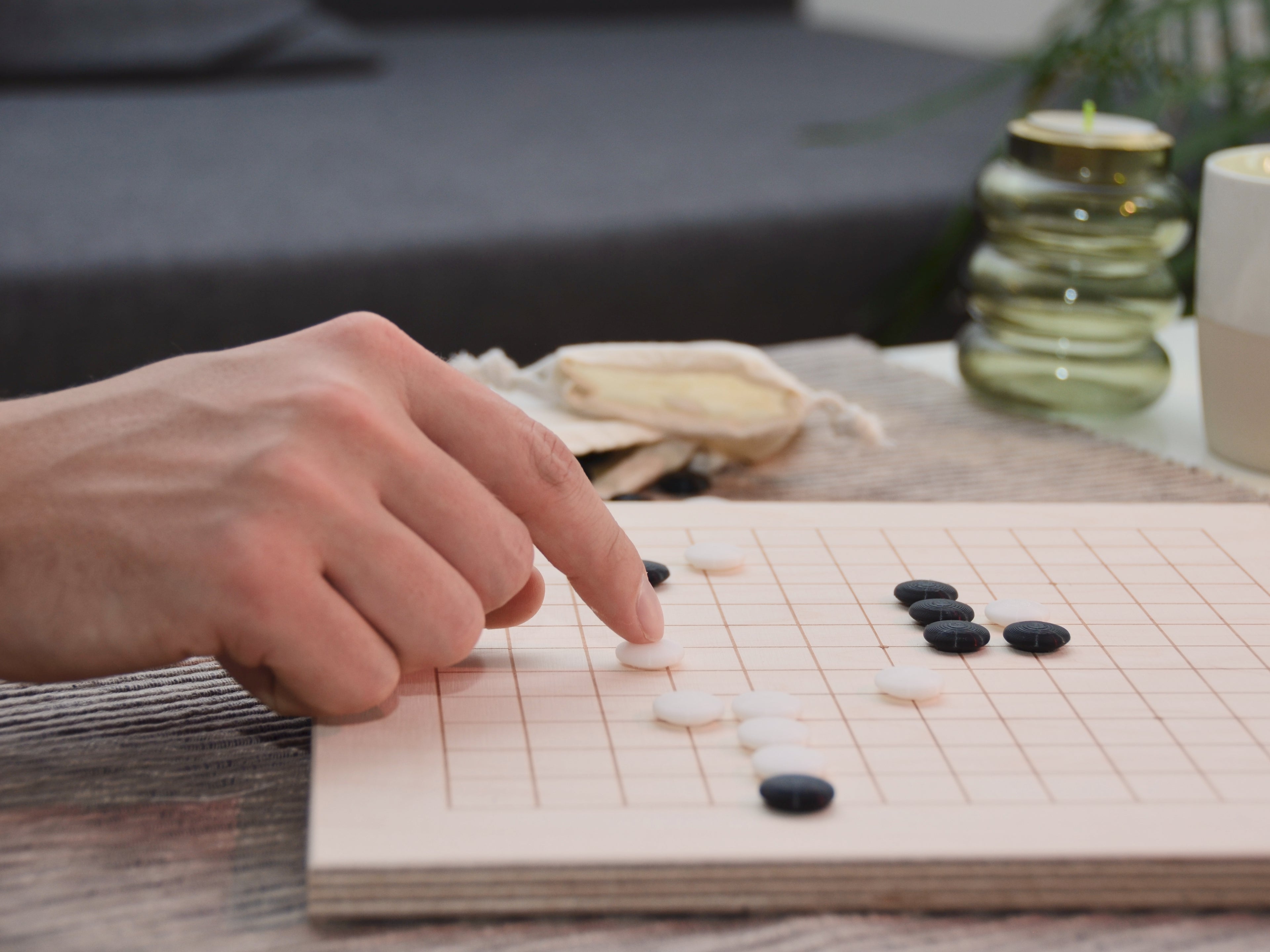 Person spielt Go auf Holzbrett: Hand platziert weißen Stein auf dem lasergravierten Holz-Spielfeld.