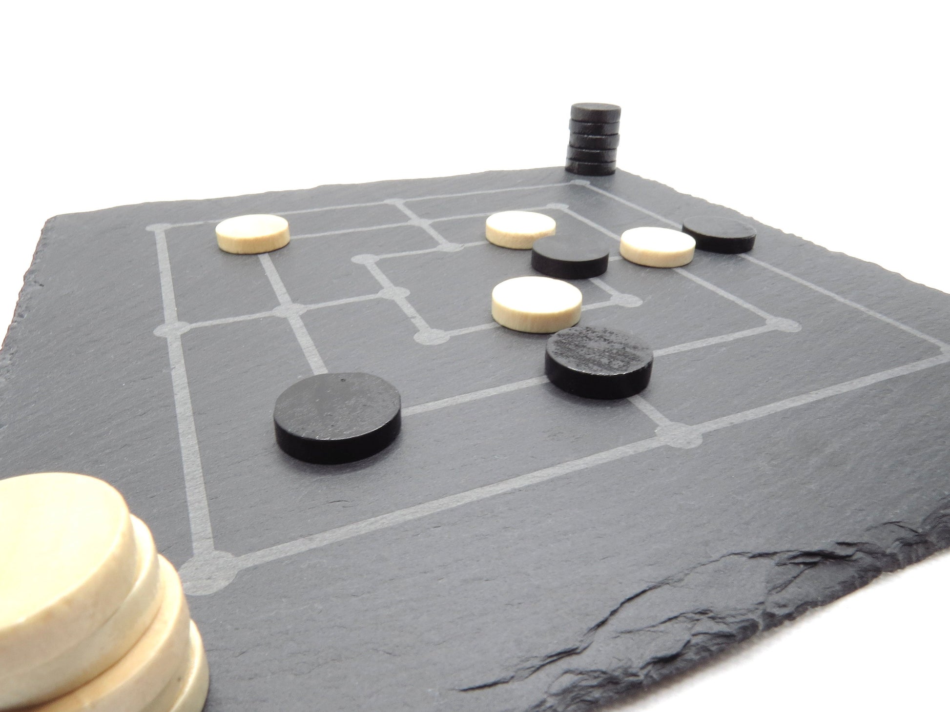Aufgebautes Mühle-Brettspiel auf Schieferplatte: Strategie-Klassiker mit modernen Spielsteinen in Spielsituation.